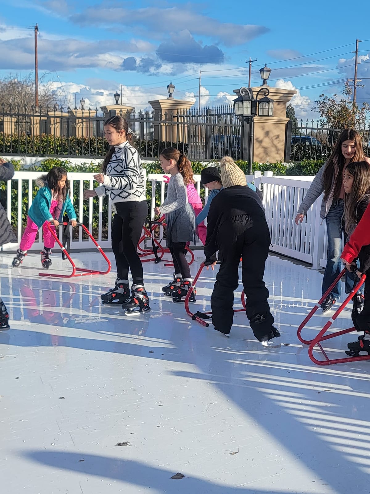 Guests skating with red skate helpers on a Custom Events synthetic ice rink surrounded by white fencing at a Sacramento-area winter event