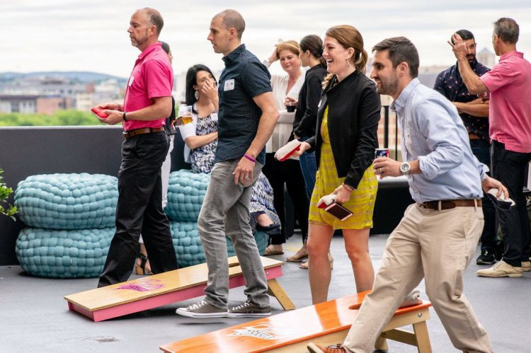 Coworkers playing cornhole lawn games at a rooftop workplace event