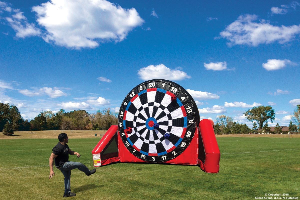 Guest kicking a soccer ball at a giant inflatable dart board game at a company picnic