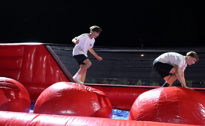 Guests crossing a red inflatable big baller attraction at an evening company event