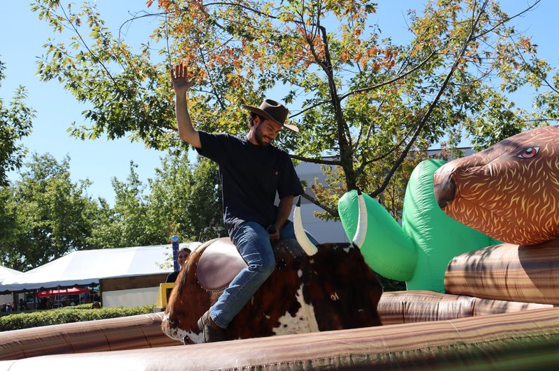 Guest riding a mechanical bull rental at a company picnic