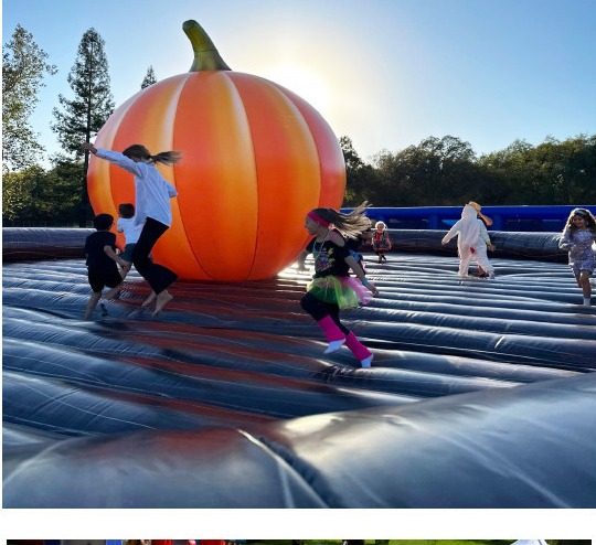 Kids jumping on a giant inflatable pumpkin attraction at a fall festival