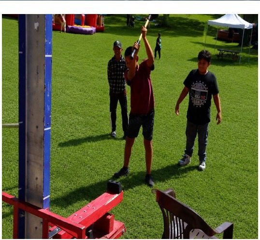 Guests playing a high striker game on the grass at a local fall event
