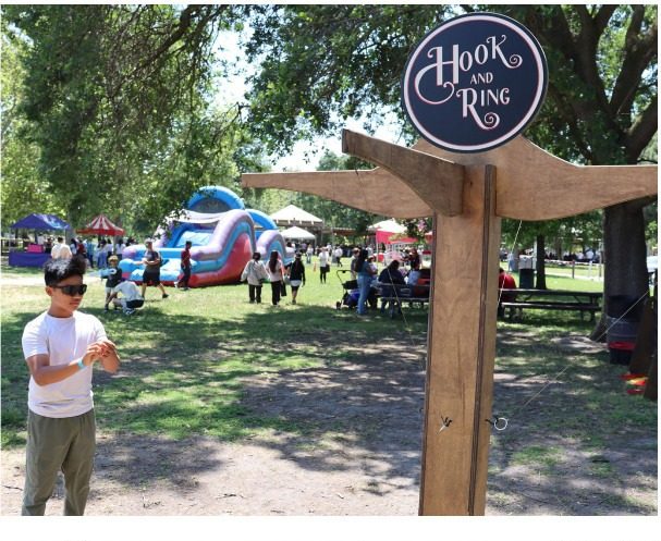 Hook and ring yard game at a shaded park event with inflatables in the background